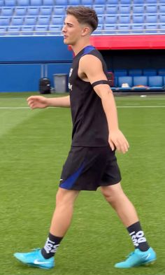 a man walking across a lush green field next to a blue stadium bleachers