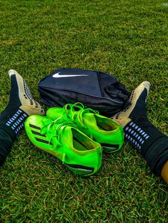 a pair of green shoes sitting on top of a lush green field next to a black bag