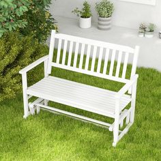 a white wooden bench sitting on top of a lush green grass covered field next to potted plants