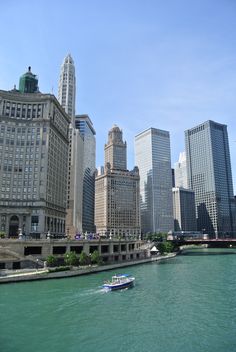 a boat traveling down the river in front of tall buildings and skyscrapers on a sunny day