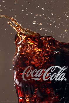 a coca - cola bottle is being poured into the water with ice and bubbles around it