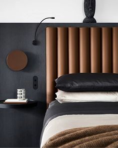 a bed with black and white sheets, pillows and a brown headboard on it