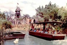 people are riding in a boat on the water near trees and a tower like structure