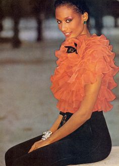 a woman sitting on the ground wearing an orange top