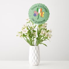 a white vase filled with flowers on top of a table next to a green sign