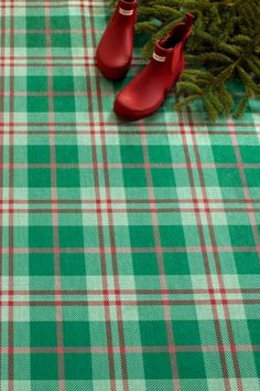 a pair of red shoes sitting on top of a green plaid table cloth next to a small christmas tree