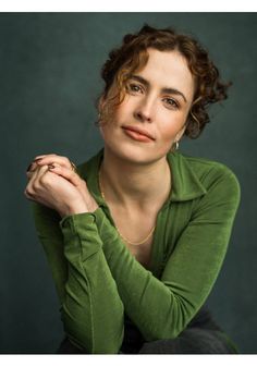 a woman with her hands on her chest posing for a photo in front of a green background