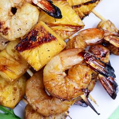 grilled shrimp and pineapple skewers on a white plate with green leaves