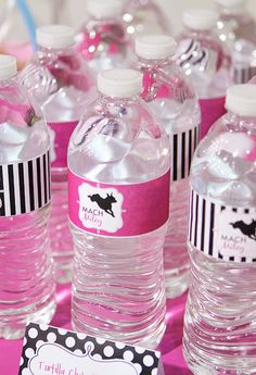 water bottles with labels on them sitting on a pink table cloth covered in black and white polka dots