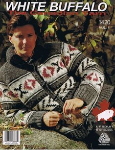 a man sitting on top of a rock next to a tree and wearing a sweater