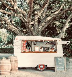 a food truck parked under a large tree next to two barrels and a chalkboard sign