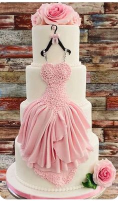 a three tiered wedding cake with pink flowers on it and a dress hanging from the top