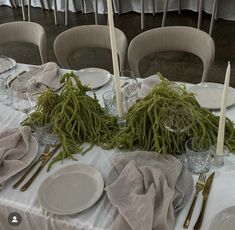 the table is set with white plates, silverware and green moss covered napkins