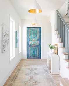 a blue door is in the middle of a hallway with stairs and rugs on the floor