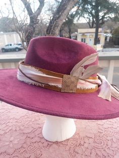 This hatband is gorgeous and has just a little extra added to it. The band is 22.5" x 1.5" and has adjustable ties in the back so it can fit hats from 22.5-34". The bottom layer is one of our favorite leathers, a metallic toasted bronze pink. Very subtle but gorgeous! The designer has then used two types of silk ribbons that complement the leather and really bring the color to life. The brown suede lace adds a nice complete to complete the top layer. As if that wasn't enough...we have added a sm Adjustable Country Hat Bands For Fall, Adjustable Short Brim Top Hat For Rodeo, Handmade Adjustable Brimmed Fedora, Adjustable Top Hat With Short Brim For Kentucky Derby, Country Style Adjustable Felt Hat With Short Brim, Adjustable Hat Bands For Country Events In Fall, Adjustable Top Hat For Kentucky Derby, Adjustable Fedora For Country Events, Adjustable Felt Hat For Kentucky Derby Country Events