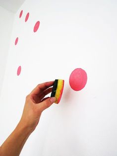 a hand is holding a sponge and pointing to the wall with red dots on it