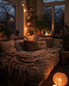 an unmade bed with lights on the windows and plants in the window sill