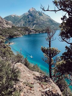 there is a boat that is in the water near some trees and mountains with blue water