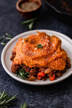 a white plate topped with lasagna covered in sauce and herbs next to a bowl of seasoning