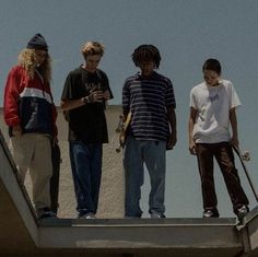 four young men standing on the edge of a building with skateboards and poles in their hands