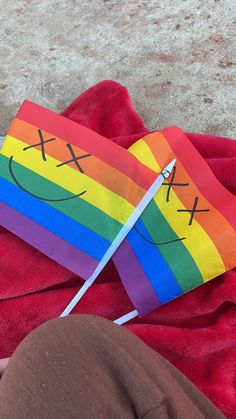 a rainbow kite laying on top of a red blanket next to a persons feet and legs