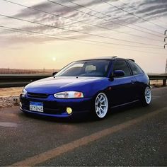 a blue car is parked on the side of the road near power lines and an overcast sky