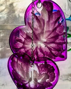 two purple heart shaped glass hangings in front of a window with flowers on them