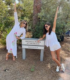 two women in white dresses standing next to a sign