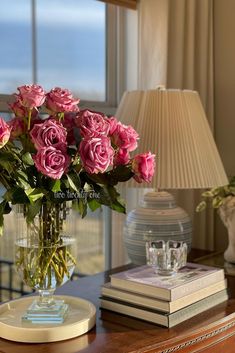 a vase filled with pink roses sitting on top of a table next to a lamp