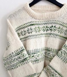 a sweater hanging on a hanger next to a white wall with green and blue designs