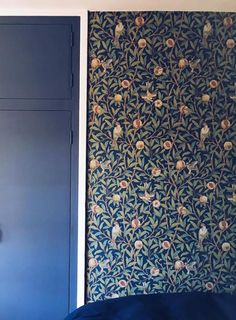 a bedroom with blue walls and wallpaper that has flowers on it, next to a bed