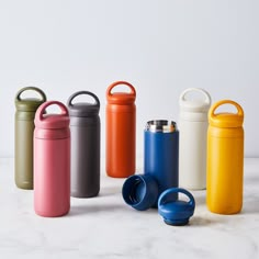 thermos are lined up in different colors and sizes, including one with an insulated lid