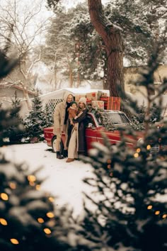 two people standing in front of a red truck with christmas decorations on it's hood