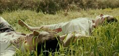 two people laying on the ground in tall grass