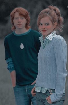 two young people standing next to each other in the grass and one is wearing a sweater