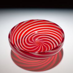 a red and white striped glass bowl sitting on top of a table next to a black background