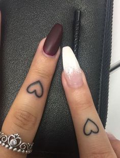 two fingers with hearts tattooed on them, one has a ring and the other has a diamond