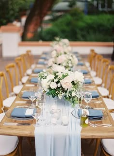 a long table set with blue and white linens, place settings and flowers on it