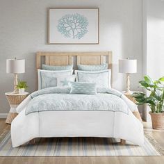 a bed with white and blue comforters in a bedroom next to a plant on the floor