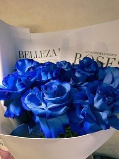 a bouquet of blue roses sitting on top of a white paper bag in someone's hand