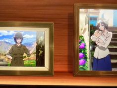 two framed pictures of anime characters on a wooden shelf next to each other, one holding a baby while the other holds an infant