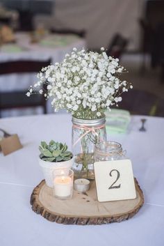 a table topped with a vase filled with white flowers and candles next to a wooden slice