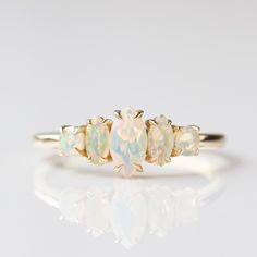 an opal and diamond three stone ring in yellow gold, set on a white background