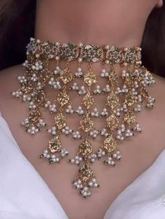 a woman wearing a gold and white necklace with pearls on the bottom of her neck