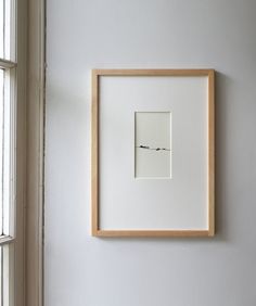 a white wall with a wooden frame hanging on it's side next to a window