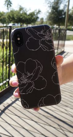 a person holding an iphone in their hand with flowers on the back and black background