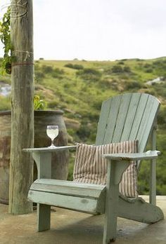 a wooden chair sitting on top of a patio next to a table with a glass of wine