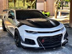 a white and black chevrolet camaro parked in front of a building with palm trees