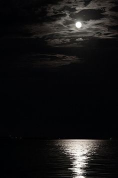 the full moon shines brightly in the night sky over the ocean with dark clouds