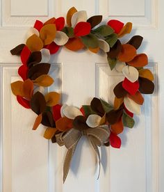 a wreath made out of felt leaves on a white door with a ribbon hanging from it